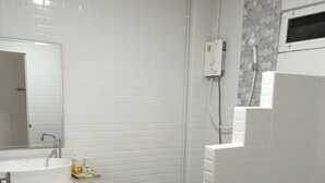 Ein Badezimmer mit weißen Fliesen, einem Waschbecken mit Seifenspendern, einer Duschkabine und einer Toilette.