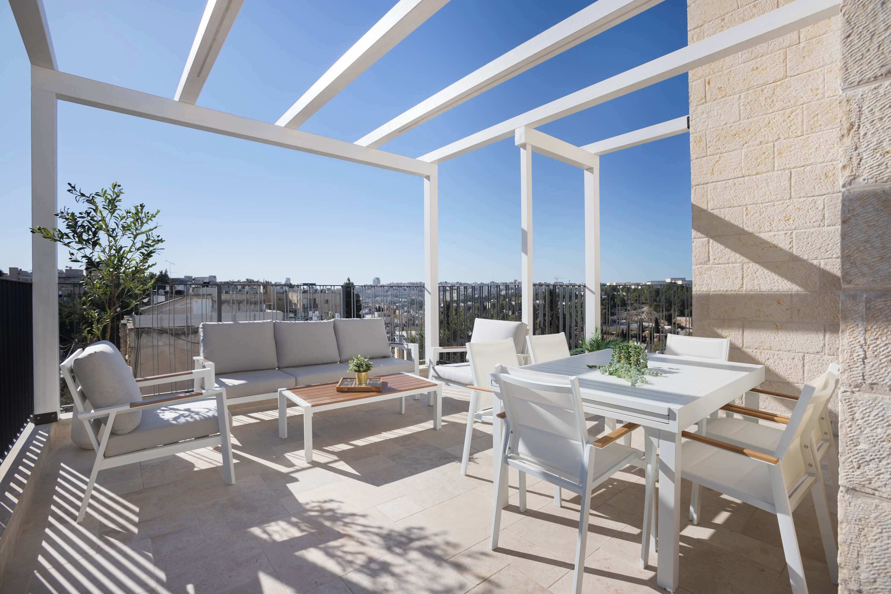 A rooftop terrace with a white table and chairs, a sofa, and a potted plant.