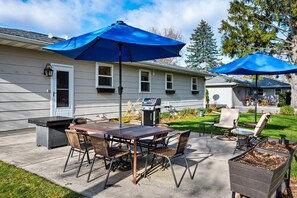 An outdoor patio with a dining table, chairs, and two blue umbrellas. - Drop Anchor | Door County Cozy Ranch Home (Sturgeon Bay)