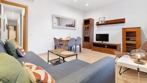 A modern living room with a sofa, a dining table with chairs, a TV, and built-in shelving.
