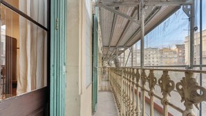 A corridor with a metal railing, a green door, and a view of buildings in the background.
