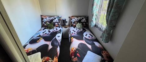 A room with two beds, each with panda-themed bedding, a shelf with items, and a window with curtains.