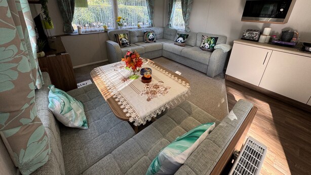 A cozy living area with a sofa set, a dining table with a floral table runner, and a kitchen area with a microwave. - Wl34 Caravan Haggerston Castle Private Decking (Berwick-upon-Tweed)
