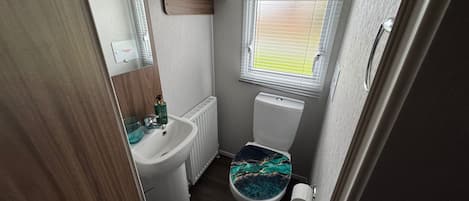 A compact bathroom with a white sink, toilet, and window with blinds.