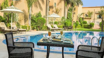 Un espace aménagé au bord de la piscine, avec des chaises longues, une table où sont servis des boissons et des palmiers.
