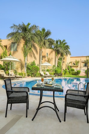 Un espace aménagé au bord de la piscine, avec des chaises longues, une table où sont servis des boissons et des palmiers.