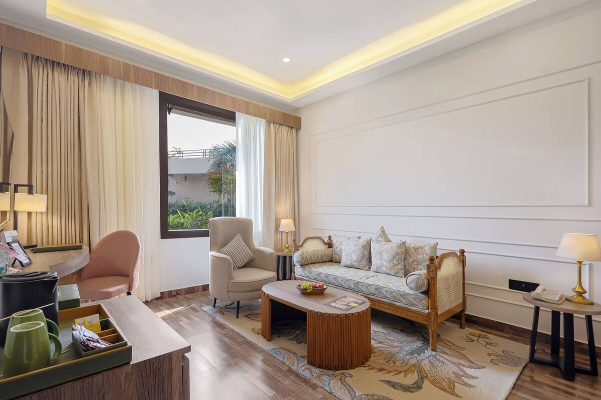 A hotel room with a sofa, armchair, coffee table, and a desk with a lamp.