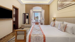 A hotel room with a large bed, a TV, a seating area with a chair, and a view of the outdoors. - Sterling Bagh Ranthambore (Sawai Madhopur)