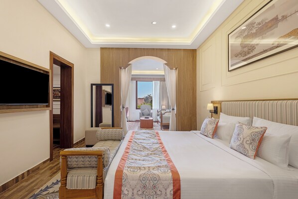 A hotel room with a large bed, a TV, a seating area with a chair, and a view of the outdoors. - Sterling Bagh Ranthambore (Sawai Madhopur)