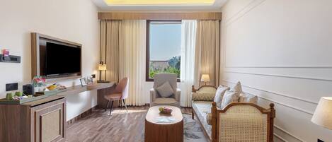 A hotel room with a flat-screen TV, a desk with a computer, a comfortable sofa, a chair, and a bed with a canopy.