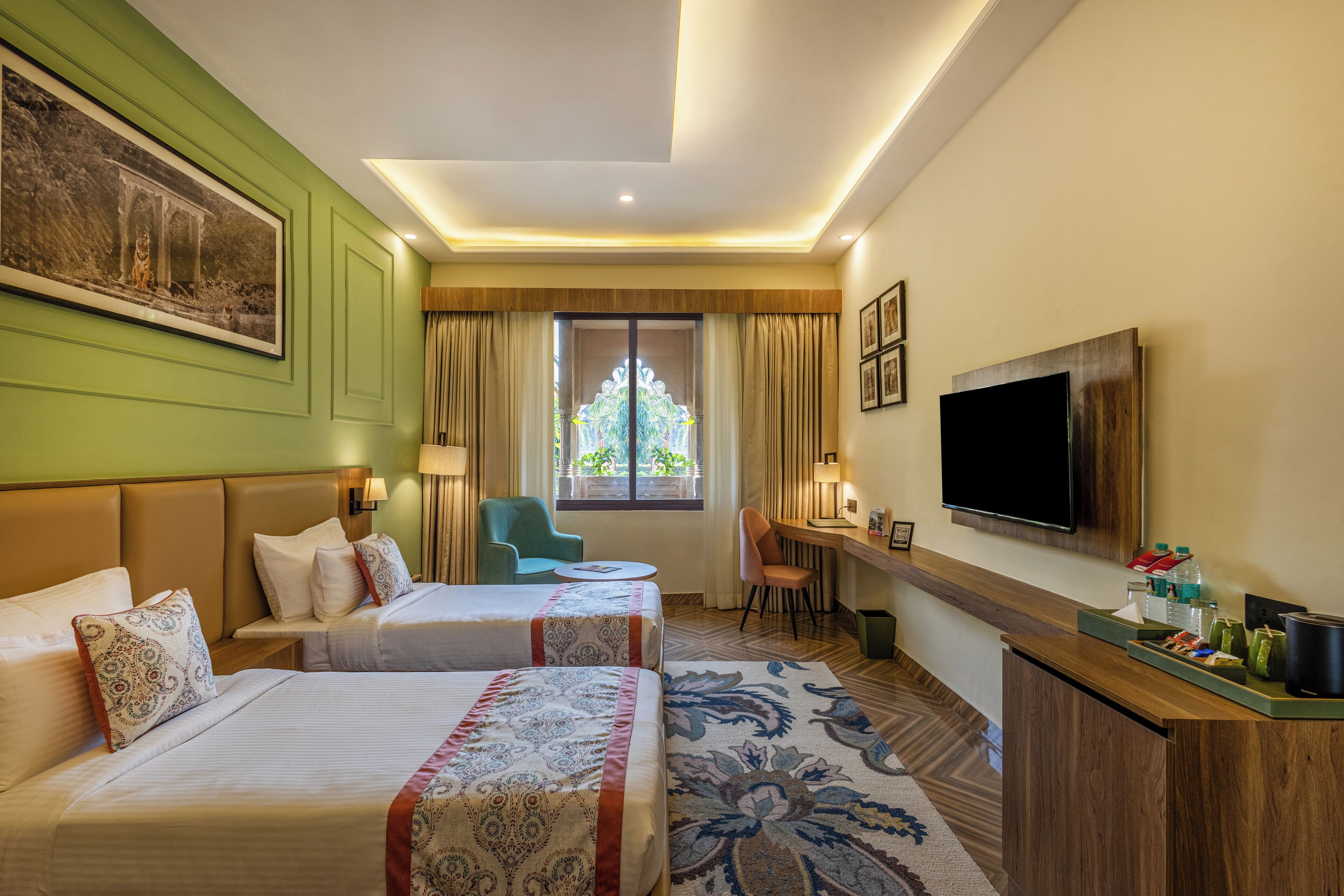 A hotel room with two beds, a desk, a TV, and a window with curtains.