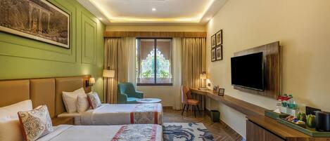 A hotel room with two beds, a desk, a TV, and a window with curtains.