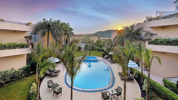 A pool area with lounge chairs, palm trees, and a sunset view. - Sterling Bagh Ranthambore (Sawai Madhopur)