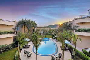 A pool area with lounge chairs, palm trees, and a sunset view. - Sterling Bagh Ranthambore (Sawai Madhopur)