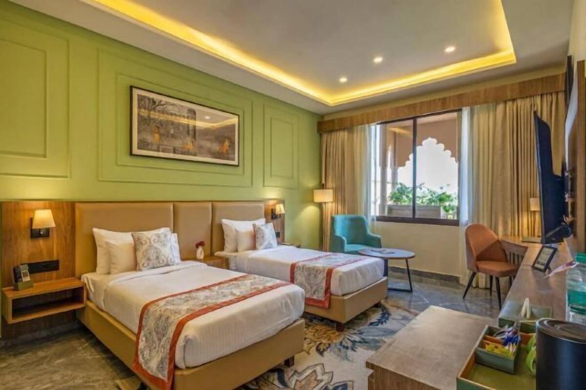 A hotel room with two beds, a desk, a chair, and a window with curtains.