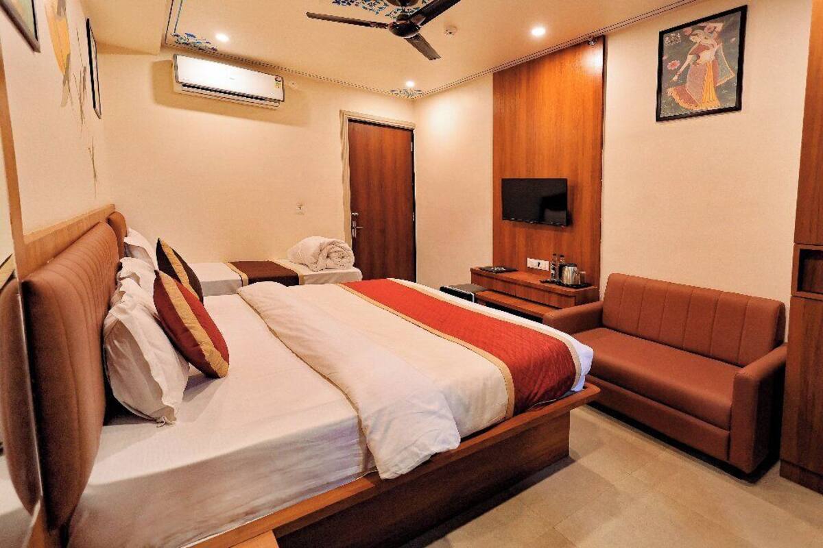 A hotel room with a bed, a sofa, a television, and a wooden wardrobe.