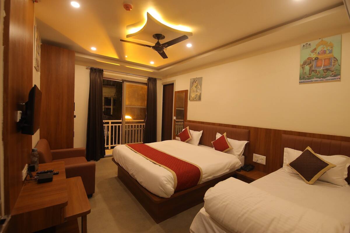 A hotel room with a large bed, a smaller bed, a desk, and a ceiling fan.