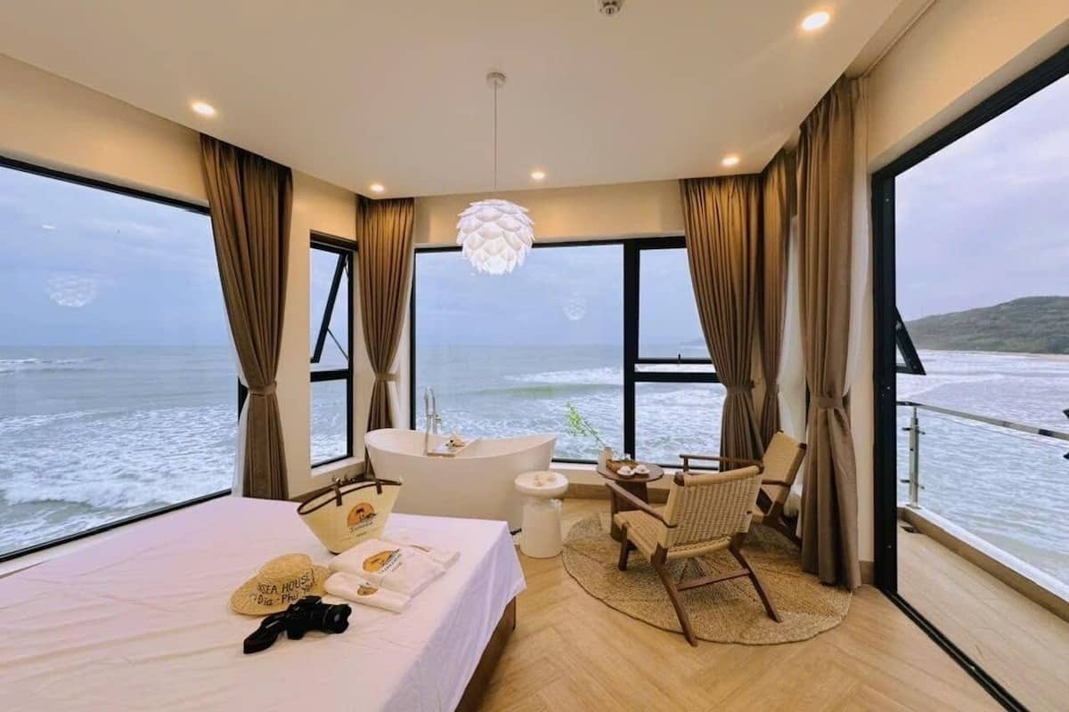 A bedroom with a large bed, a bathtub, a chair, and a view of the ocean.