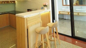Une cuisine moderne dotée d’un îlot central, de luminaires suspendus et d’une porte en verre donnant sur une salle de bain.