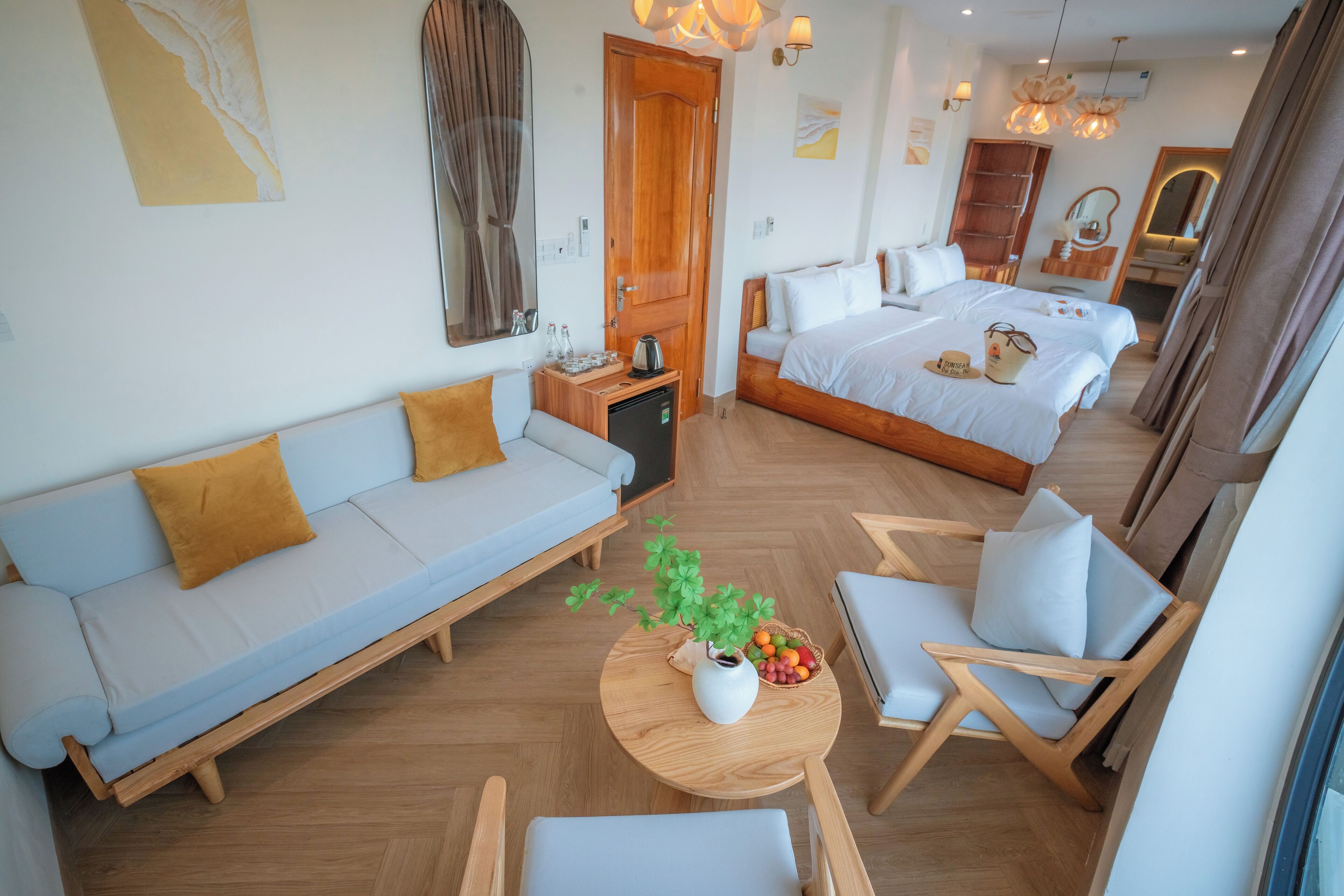 Een moderne hotelkamer met een bank, twee eenpersoonsbedden, een eettafel met stoelen, een kleine keukenhoek en een grote spiegel.