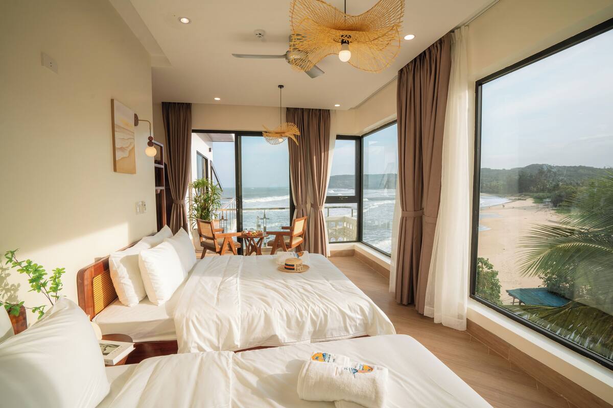 A spacious bedroom with a large bed, a dining area, and a view of the beach.
