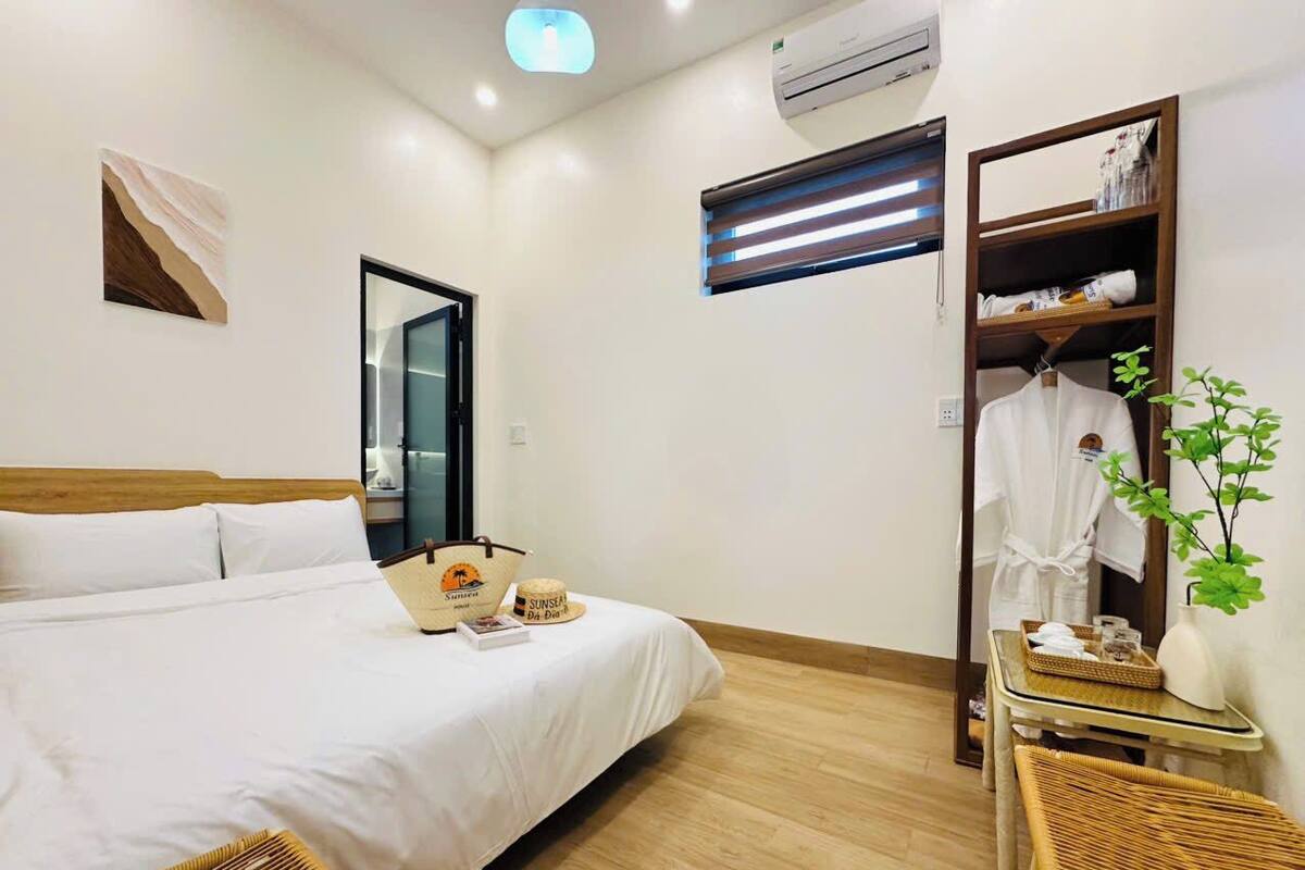 A hotel room with a bed, a wardrobe, a mirror, a small table, and a plant.