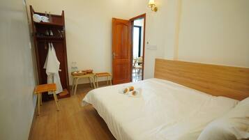 Un dormitorio con cama de madera, un armario de madera, una mesita con una silla y una puerta que da a otra habitación.