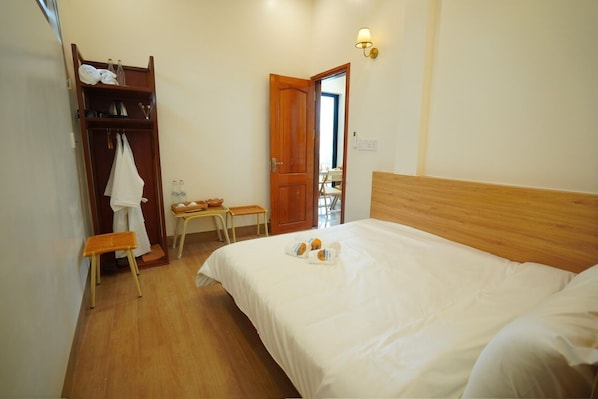 A bedroom with a wooden bed, a wooden wardrobe, a small table with a chair, and a door leading to another room.