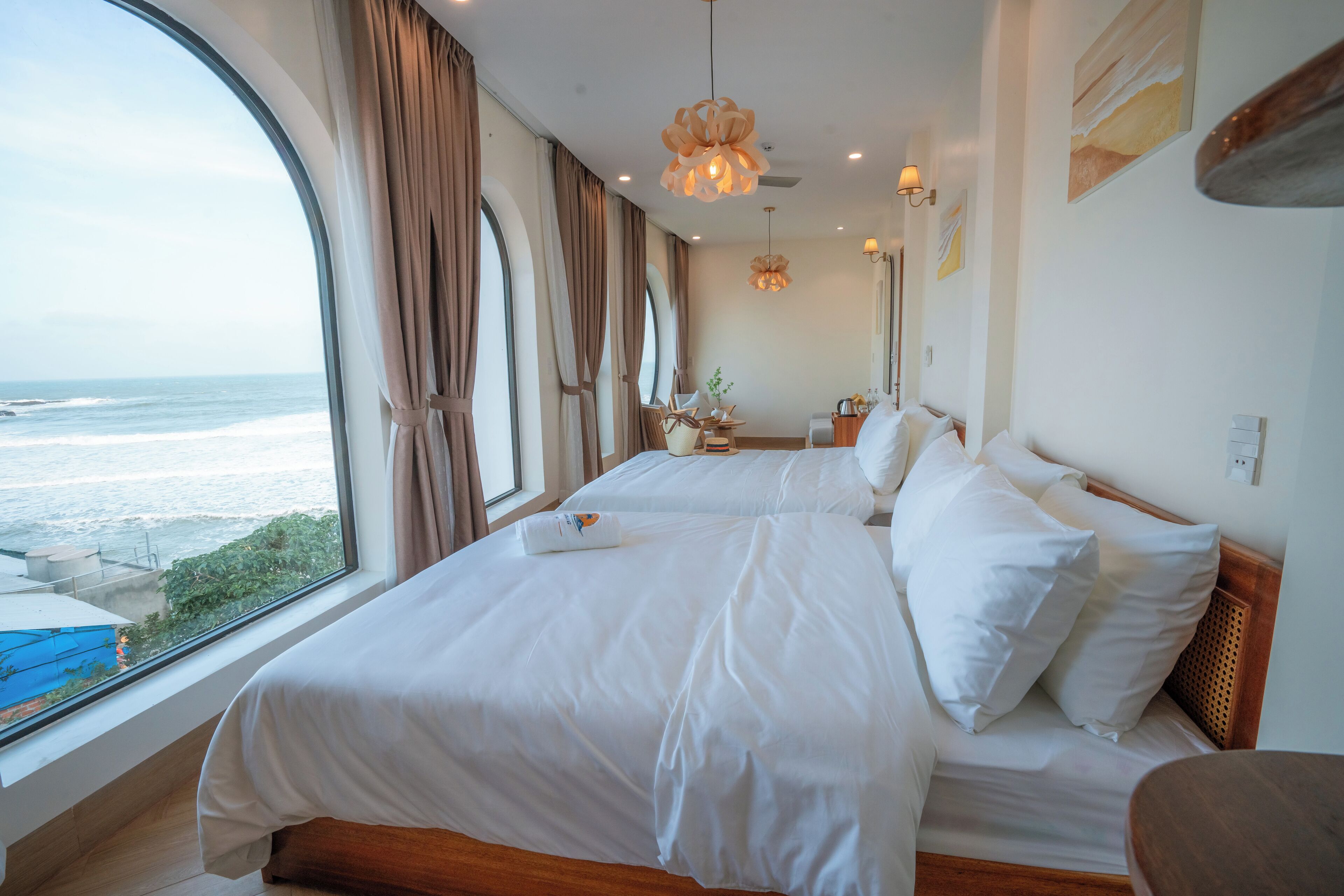 A hotel room with two beds, large windows with ocean views, and modern decor.