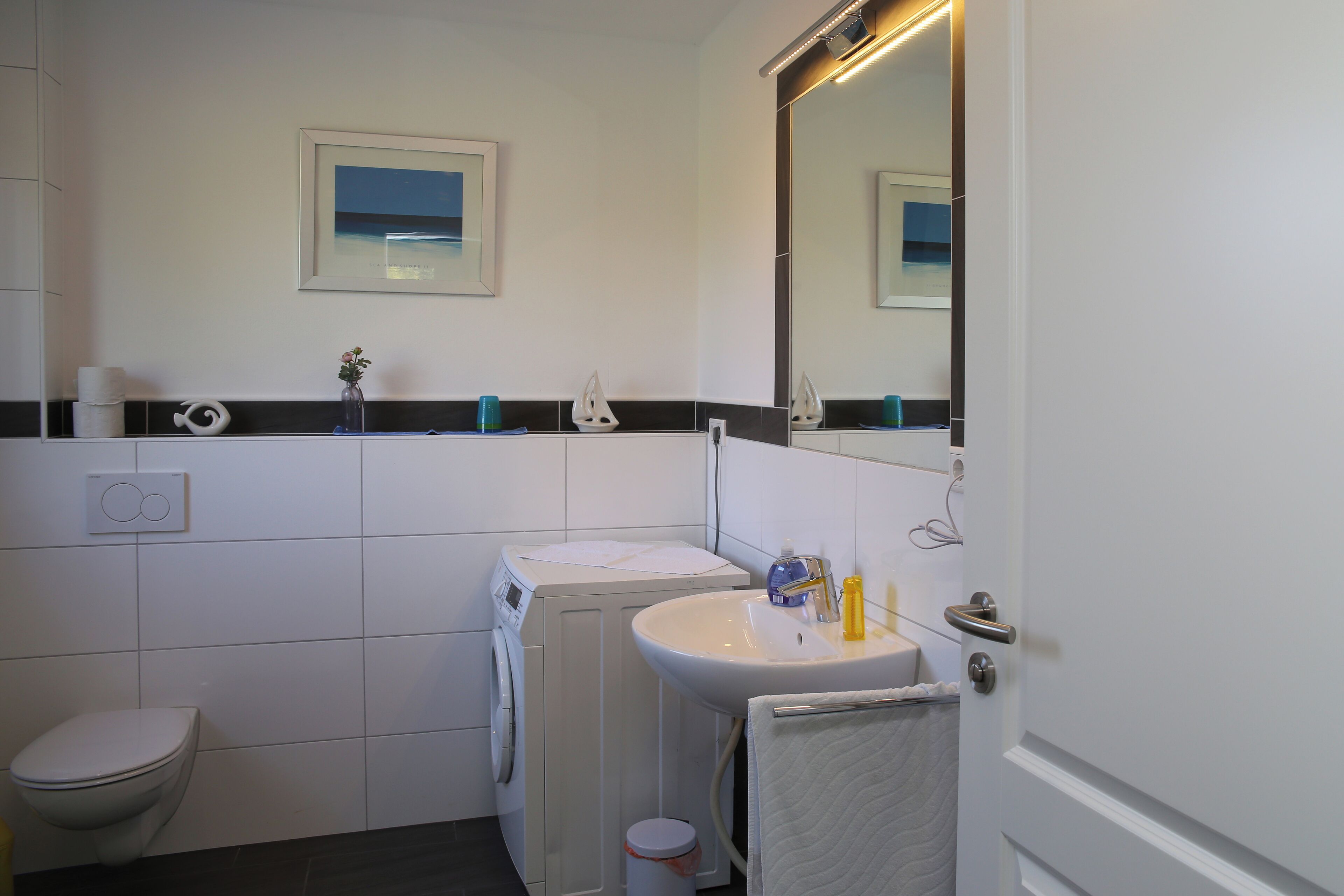 A bathroom with a toilet, washing machine, sink, and a mirror.