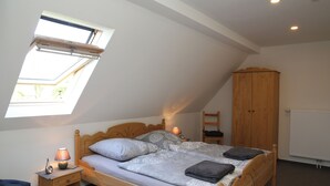 Une chambre avec un plafond en pente, un puits de lumière, un lit en bois, une table de chevet avec une lampe, une armoire et un radiateur.