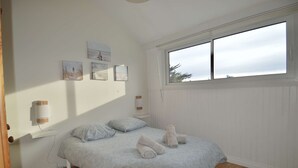 A bedroom with a bed, two pillows, a window, and wall art. - Aux beaux coquillages, sea and harbor view (Courseulles-sur-Mer)