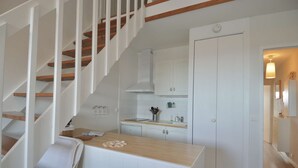 A modern kitchen with white cabinetry, a wooden countertop, and a staircase with white railings. - Aux beaux coquillages, sea and harbor view (Courseulles-sur-Mer)