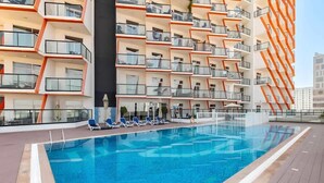 Een modern hotel met een dakzwembad, meerdere balkons en een heldere lucht.