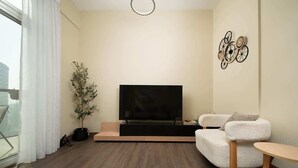 Een moderne woonkamer met een flatscreen televisie, een witte bank, een bijzettafeltje en een potplant.