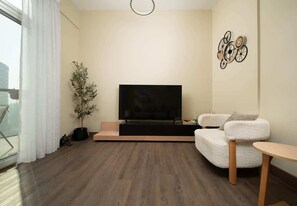 A modern living room with a flat-screen TV, a white sofa, a small table, and a potted plant. - Dubai Al Jaddaf Apt Pool Gym Free Parking (Dubai)