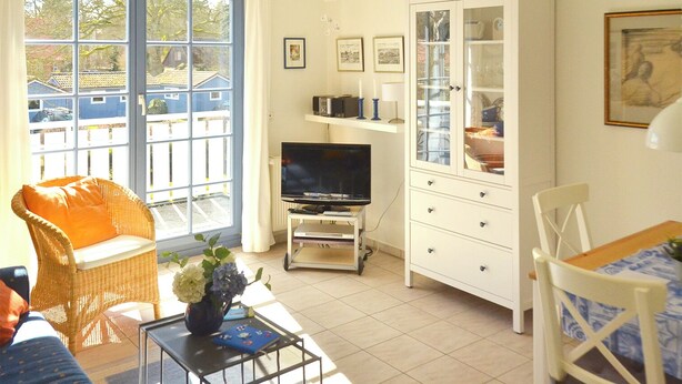 A living room with a television, wicker furniture, a cabinet with glass doors, and a view of the outside. - Quiet, wooded apartment in Eichenpark Prerow, 2 pers., WLAN, south-west-facing balcony (Ostseebad Prerow)