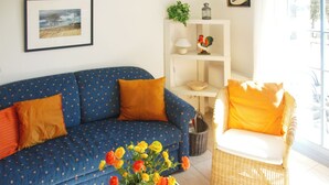 A living room with a blue sofa, orange cushions, a wicker chair, and a vase of flowers. - Quiet, wooded apartment in Eichenpark Prerow, 2 pers., WLAN, south-west-facing balcony (Ostseebad Prerow)