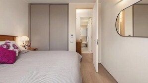 Una habitación de hotel moderna con una cama, una mesita de noche, un espejo y una puerta que da a un baño.