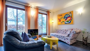 A living room with a sofa, a black leather chair, a small table, and a TV. - Apartment for 2 p. + toddler, central and close to the beach, fireplace, sauna, terrace, WLAN (Prerow)
