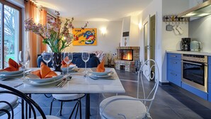 A dining area with a table set for four, a fireplace, and a kitchen with modern appliances. - Apartment for 2 p. + toddler, central and close to the beach, fireplace, sauna, terrace, WLAN (Prerow)