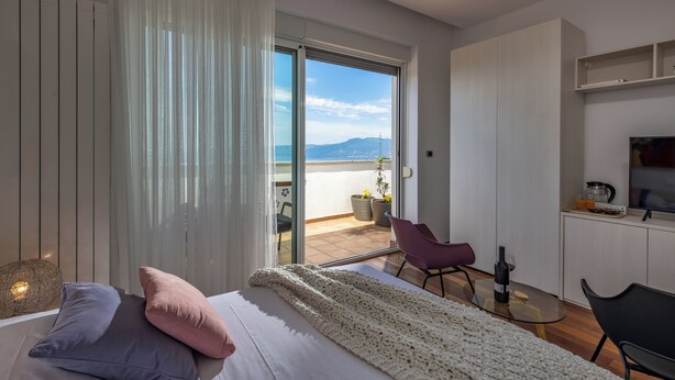 A modern bedroom with a large bed, a view of the balcony, and a small kitchenette. - Terra Magica Room with Private Parking (Cavle)