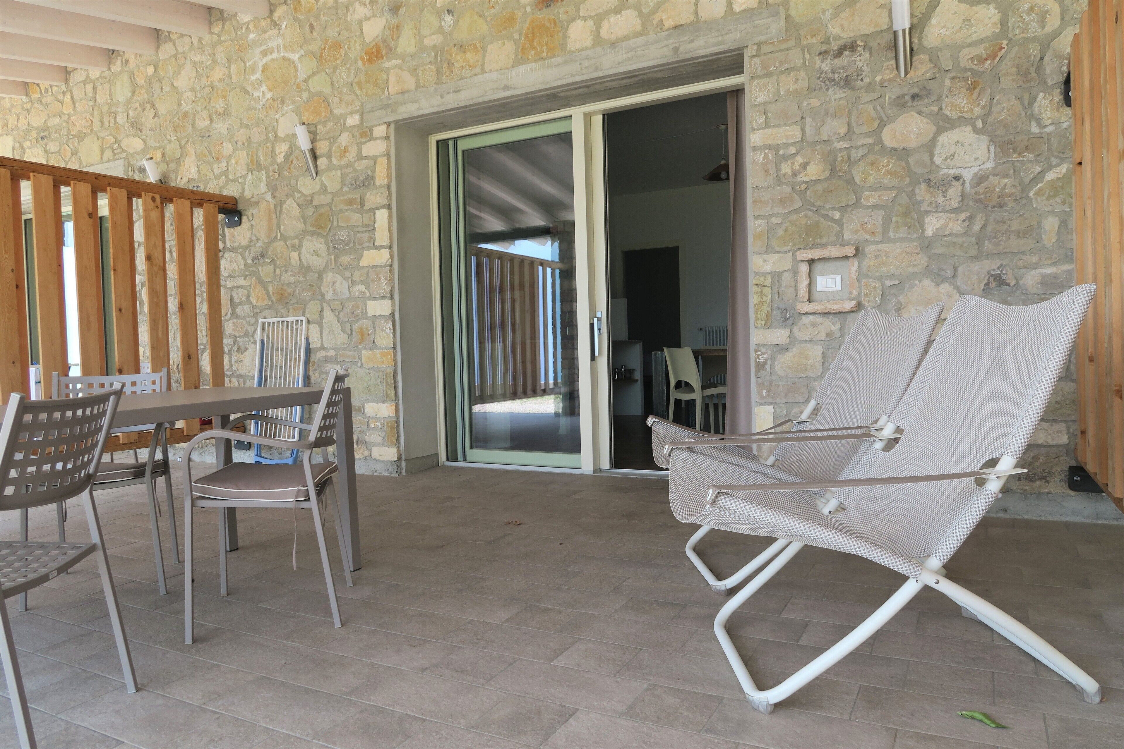 Une terrasse dallée de pierres, avec une table et des chaises, une chaise pliante et une porte-fenêtre coulissante donnant sur un espace intérieur.