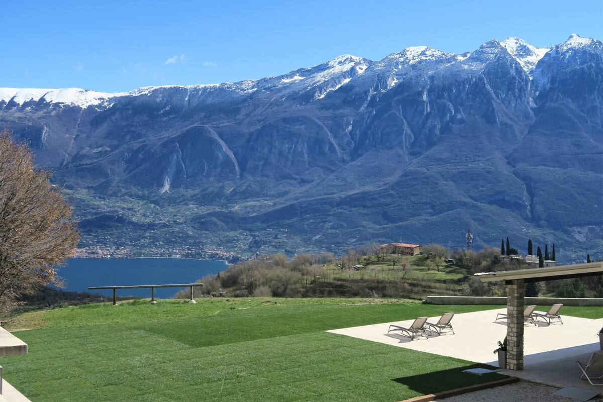 A patio with outdoor seating, a view of a lake, and snow-capped mountains in the background.