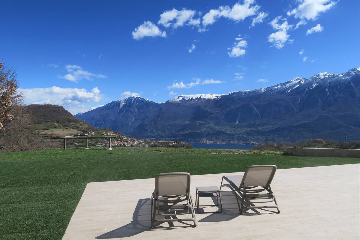 A terrace with two lounge chairs overlooking a mountainous landscape with a lake.