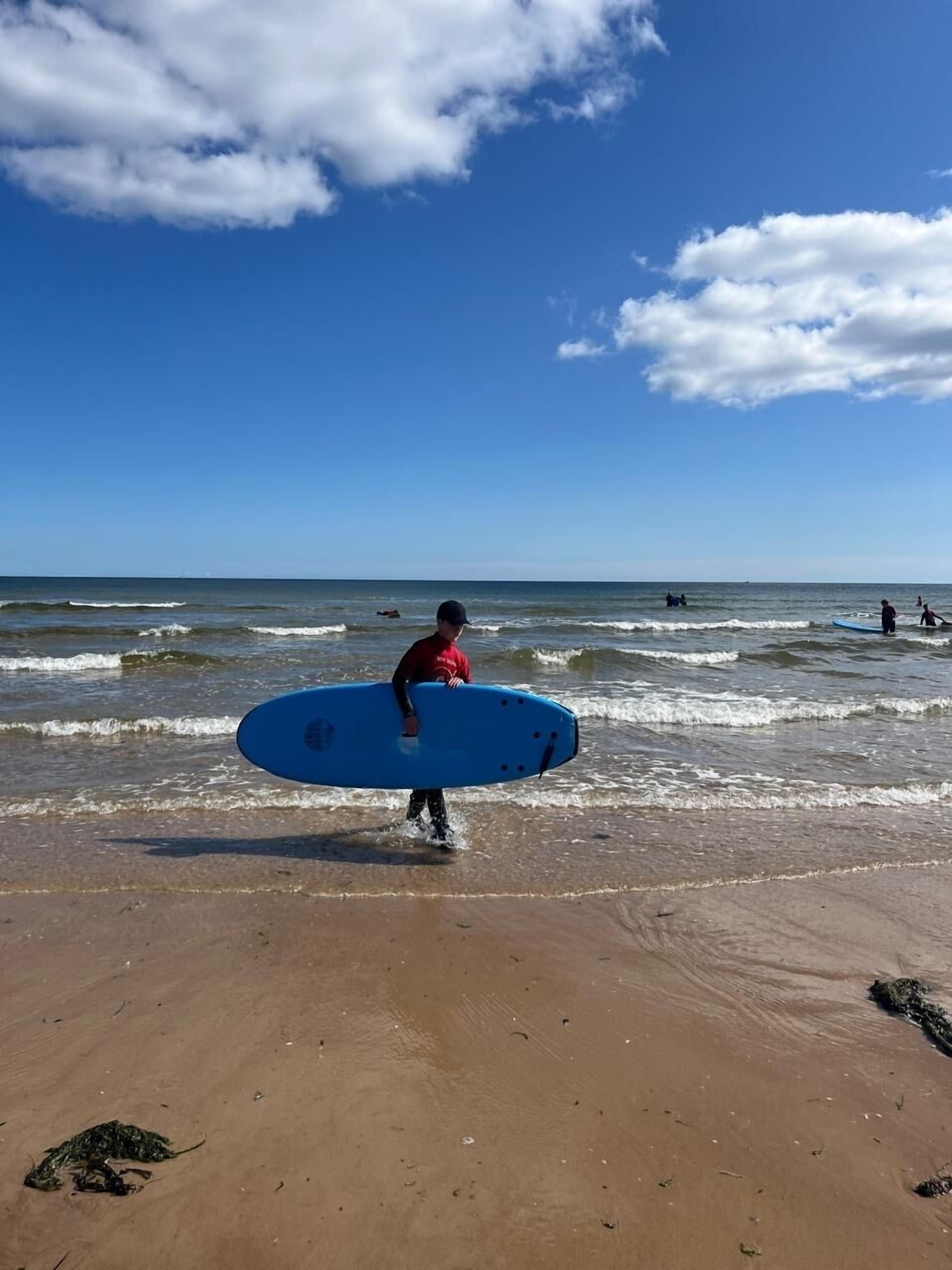 A beach scene with a person carrying a blue surfboard.