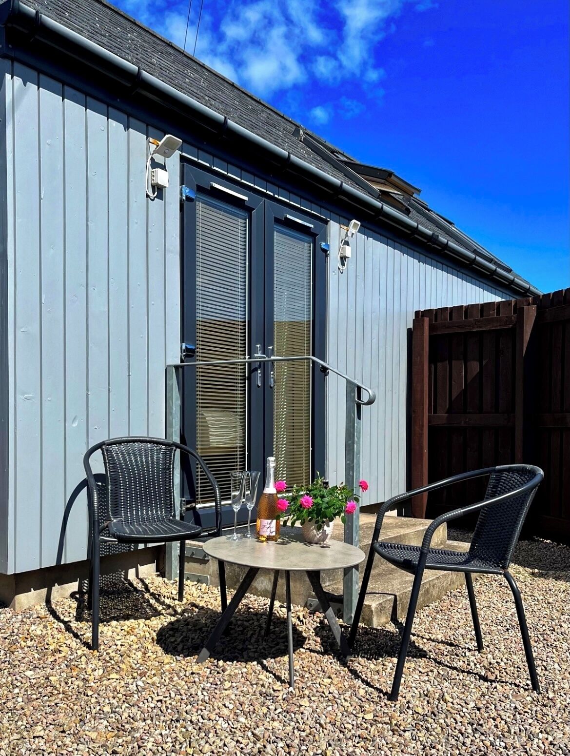 Une terrasse avec deux chaises, une table et une bouteille de vin.