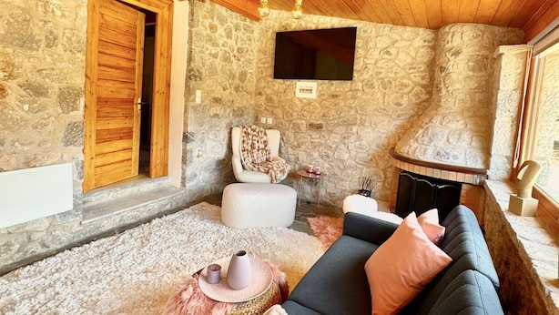 A cozy living room with a stone wall, wooden ceiling, and a fireplace.
