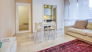 A modern living room with a beige sofa, a dining table with chairs, a red patterned rug, and a kitchen visible through an open door. - Easylife - Exclusive Comfort in Porta Romana (Milano)