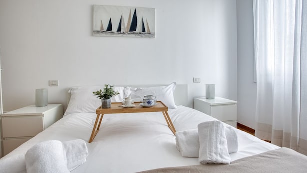 A neatly made bed with a tray of breakfast items, white bedding, and a painting of sailboats on the wall. - Easylife - Exclusive Comfort in Porta Romana (Milano)